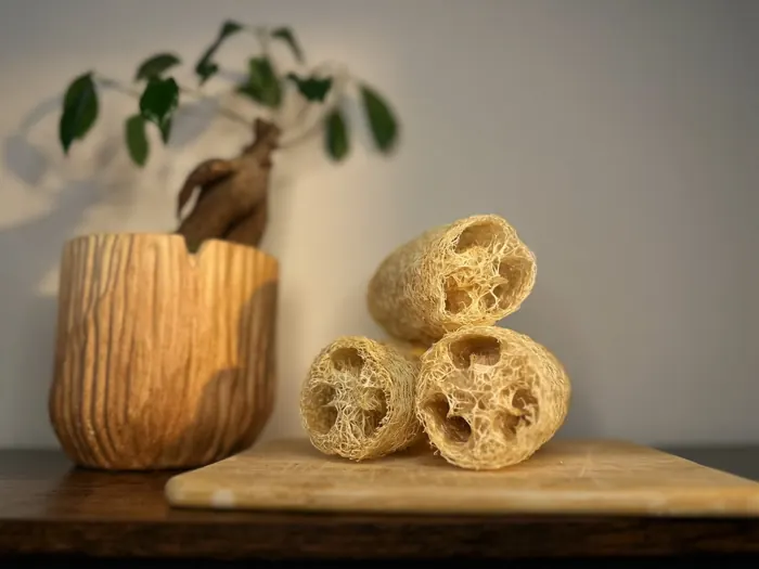 Three hand-cut luffa cutlets stacked on a wooden board beside a wooden planter