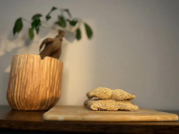 Two flat luffa scrub pads stacked on a wooden board