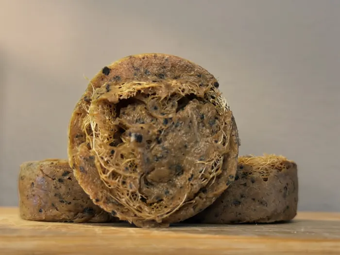 Close view of a coffee goat milk soap bar with a luffa slice set into its center