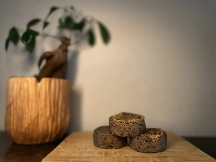 Three coffee goat milk soap bars with luffa stacked on a wooden board